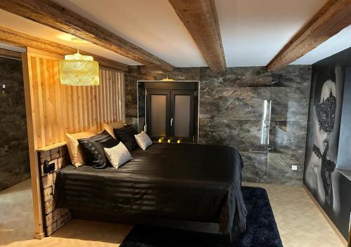 a bedroom with a black bed with a stone wall at Keriana Luxe et détente privée en Alsace in Muttersholtz