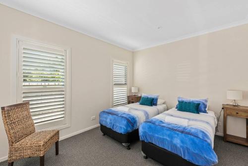 a bedroom with two beds and a chair and a window at Sunny Townhouse in Huskisson