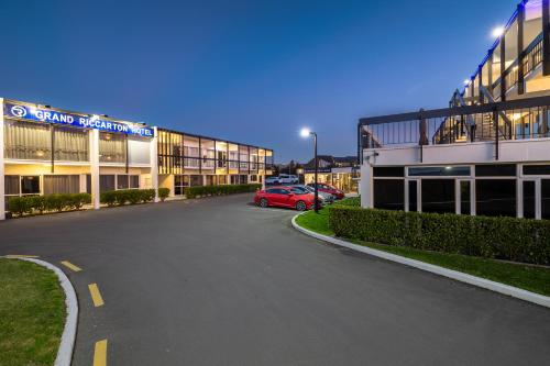 a parking lot in front of a building with a red car at Grand Riccarton Hotel in Christchurch