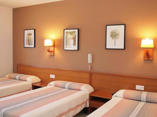 three beds in a room with three lamps on the wall at Hotel El Castell in Calafell