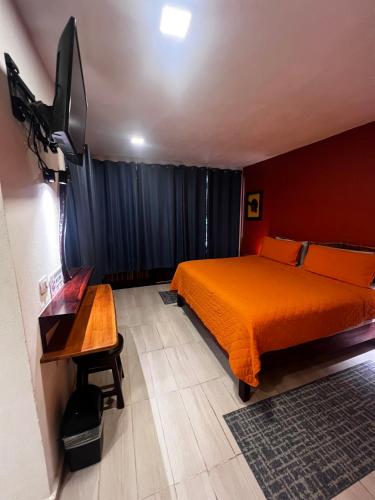 a bedroom with an orange bed and a flat screen tv at Hotel "Casa Las Lolas" in Xpujil