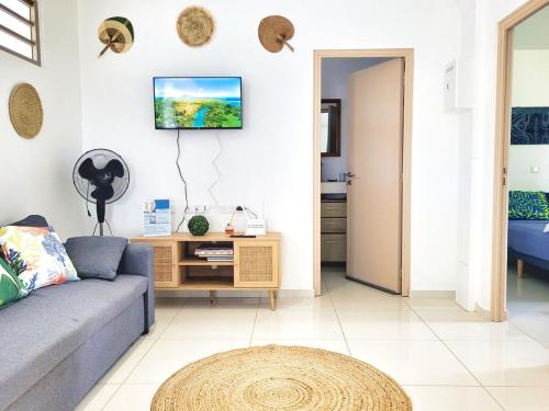 a living room with a couch and a tv on the wall at Logement de charme, au soleil et proche de la mer in Moorea