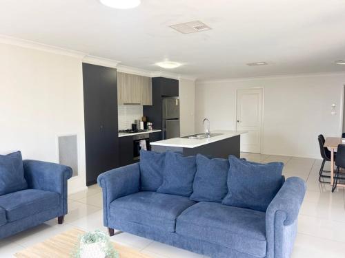 a living room with two blue couches and a kitchen at Urban 3BR Oasis: Style & Comfort in Wagga Wagga