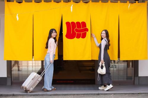 two women are standing in front of a yellow banner at UDON na HOTEL 琴平 in Kotohira