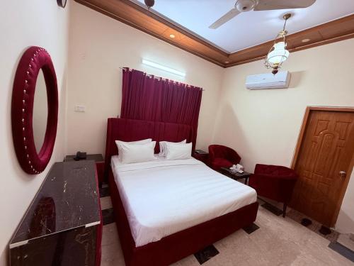 une chambre avec un lit avec une tête de lit rouge et un miroir dans l'établissement Clift Royal In, à Islamabad