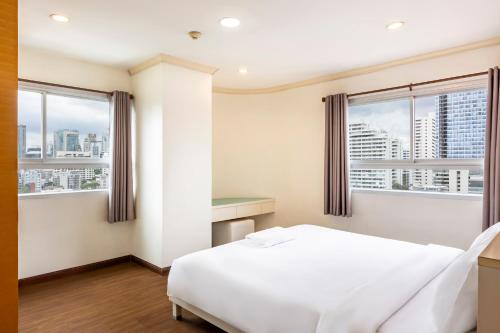 a bedroom with a white bed and two windows at Teja Hotel in Bangkok