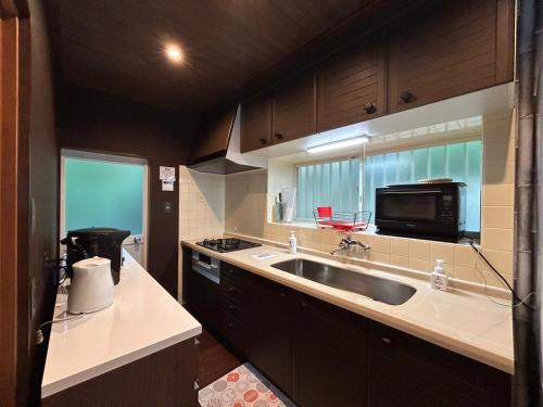 una cocina con fregadero y microondas en 温泉付き 自然に囲まれながら別荘生活を満喫 1棟貸切 湖畔 バーベキュー 長期滞在 ファミーユ伊豆の瞳, en Ito