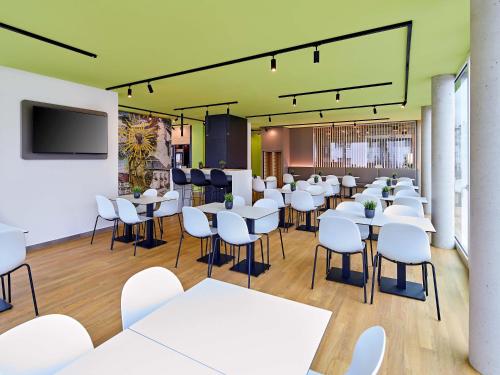 un restaurante con mesas y sillas blancas y TV de pantalla plana en B&B HOTEL Arnsberg, en Arnsberg
