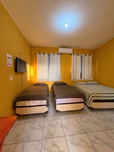 Tres camas en una habitación con paredes amarillas y un televisor. en Pousada Calçadão, en Ipueiras