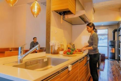 a woman standing in a kitchen preparing food at 源泉かけ流し温泉付き一棟貸しVilla Gensen Two in Yuzawa