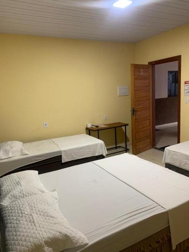 a room with two beds and a door with a table at Hotel Arara Azul in Pontes e Lacerda