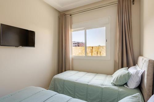 a room with two beds and a window with a television at APT-Cinema Pool-Free Parking-Gym-Netflix in El Jadida