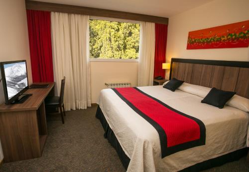 a hotel room with a bed and a desk and a window at Huinid Pioneros Hotel & Aparts in San Carlos de Bariloche