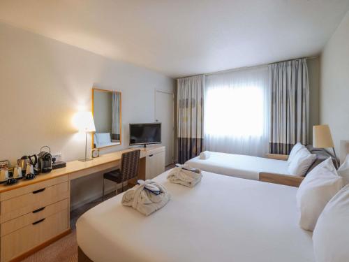 Una habitación de hotel con dos camas y un escritorio. en Novotel Milton Keynes, en Milton Keynes