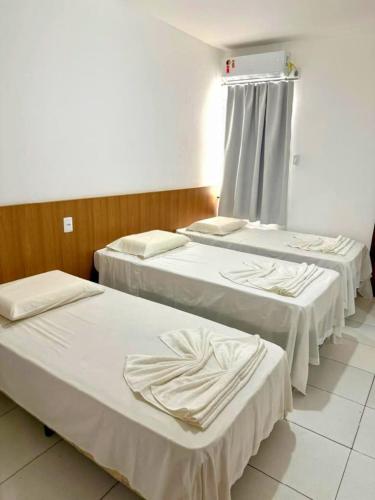 Tres camas en una habitación de hospital con sábanas blancas. en Hotel Ideal, en Jequié