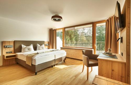 a bedroom with a bed and a desk and a window at Das Dreiburgensee Naturhotel & Spa im Bayrischen Wald in Thurmansbang