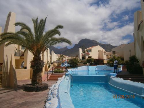 een zwembad met een palmboom en gebouwen bij Mare Verde - JOY in Adeje