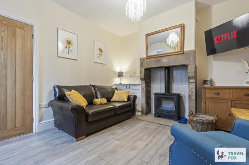 a living room with a leather couch and a fireplace at Pear Tree Cottage Pool Table 15mins drive to Alton Towers in Denstone