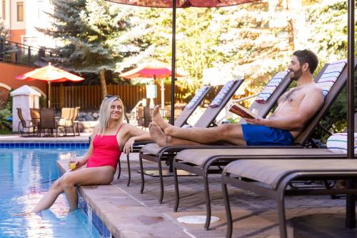a man and woman sitting on lounge chairs by a swimming pool at Montaneros in Vail in Vail