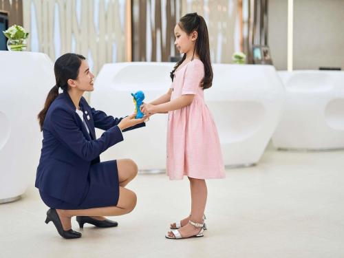 a woman is handing a little girl a brush at Novotel Hanoi Thai Ha in Hanoi