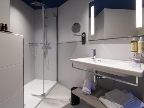 Un baño blanco con lavabo y ducha. en Maek Hotel Antwerp Central - Handwritten Collection, en Amberes