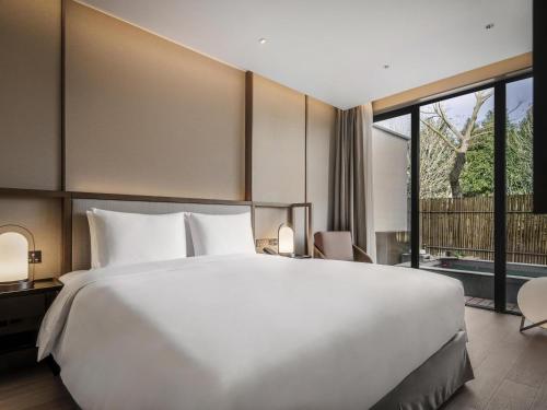 Cette chambre comprend un grand lit blanc et une grande fenêtre. dans l'établissement Ocean Spring Resort Chengdu - MGallery Collection, à Chengdu