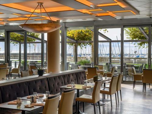 a restaurant with tables and chairs and windows at Mövenpick Hotel Lausanne in Lausanne