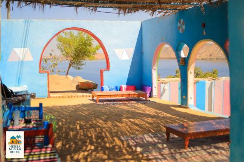 a blue building with tables and benches in front of the water at Heissa Nubian Hostel in Aswân Reservoir Colony