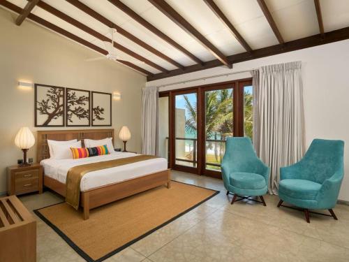 a bedroom with a bed and two blue chairs at Driftwood Villa in Pamunugama