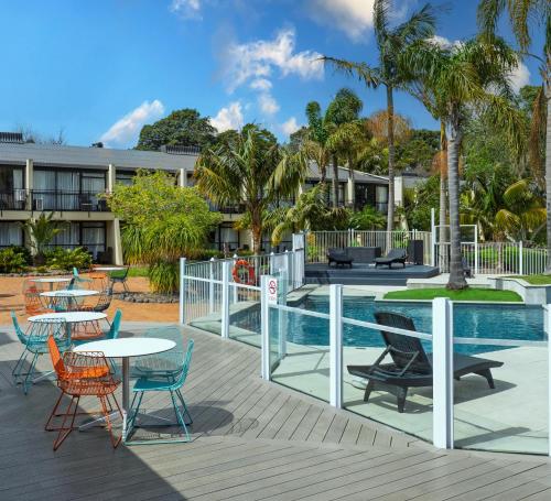 a deck with tables and chairs next to a pool at Holiday Inn Auckland Airport by IHG in Auckland