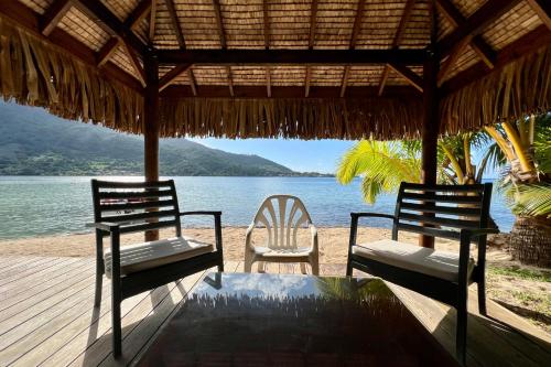 two chairs and a table on a beach with the water at Villa Ohana - 4BR Beachfront Villa in Paopao