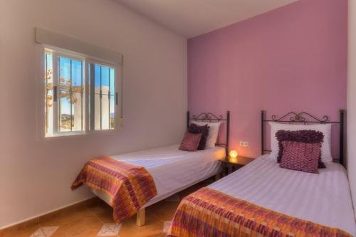 two beds in a room with purple walls and a window at Villa Damara in Albox