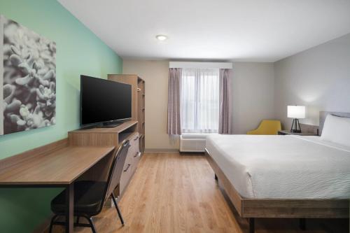 a hotel room with a bed and a desk with a television at ECHO Suites Extended Stay by Wyndham Springfield Airport PLZ in Springfield