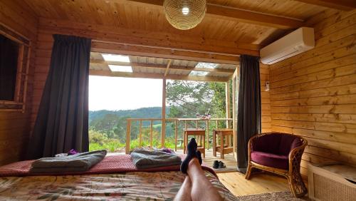 a person laying on a bed in a room with a large window at Fantail Point - secluded cabin with amazing views in Upper Papamoa