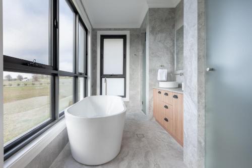 a bathroom with a large white tub and windows at The Riverside House in Burradoo