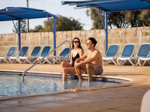 a man and woman sitting next to a swimming pool at BIG4 Breeze Holiday Parks - Busselton in Busselton