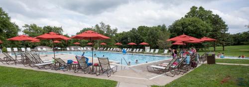 a swimming pool with chairs and red umbrellas at Circle M Camping Resort Screened Park Model in Wabank