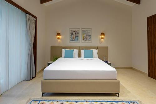 a bedroom with a large white bed with blue pillows at Lamrin Morjim Goa in Morjim
