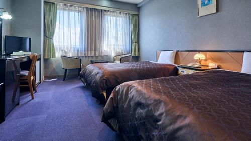 a hotel room with two beds and a desk at Hotel Satsukien in Kanoya