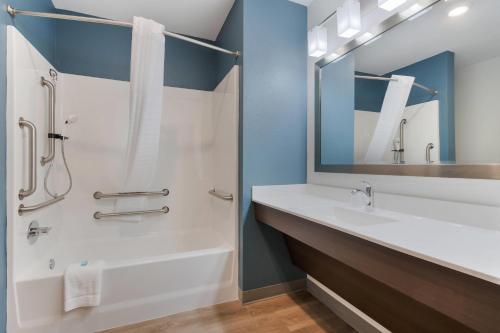 a bathroom with a sink and a shower with a mirror at WoodSpring Suites Tamarac in Tamarac