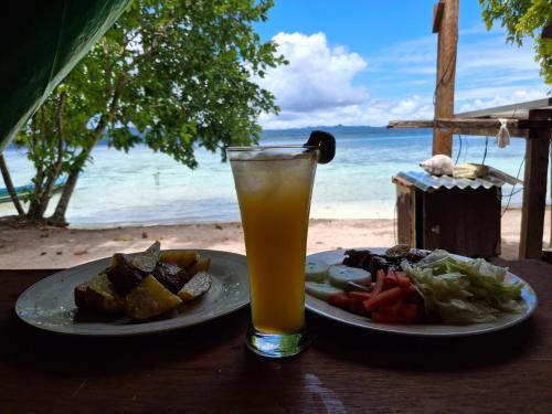 KriにあるEddo Homestayのビーチに面したテーブルの上には2枚の食べ物と飲み物が並んでいる