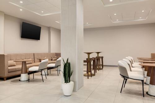 Una sala de espera con sillas y mesas y un televisor. en Wyndham Garden Atlanta Airport, en Atlanta