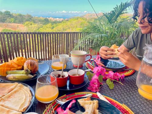 a woman sitting at a table with breakfast foods at Appartement YLANG in Hell-Ville