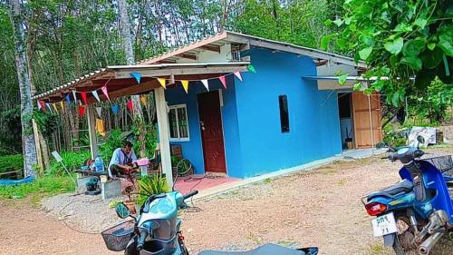 a man sitting at a table in front of a blue house at Abu Sea Man House in Ko Lanta Yai