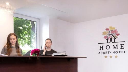 Dos mujeres sentadas en un escritorio en una habitación en HOME Apart-Hotel Vilnius, en Vilna