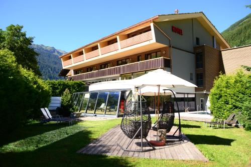 a building with an umbrella and chairs in front of it at Hotel Rovanada Wellness & BergNatur in Vals