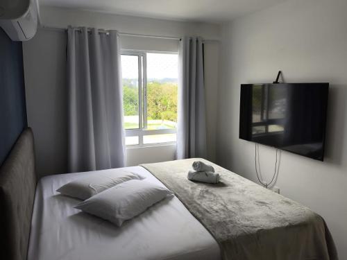 una camera da letto con un letto, una TV e una finestra di Apartamento 2 quartos Blumenau a 10 minutos da Vila Germânica a Blumenau