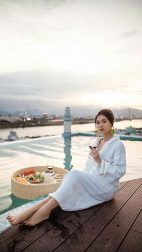 a woman in a white dress sitting next to a pool at Infinity Pink Hotel Riverview in Danang