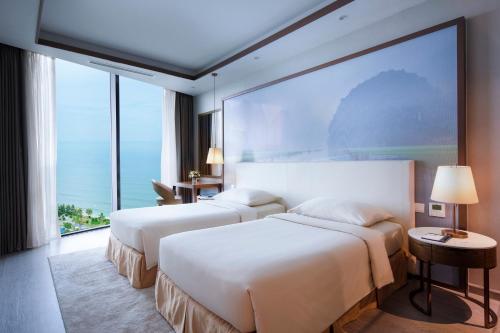 two beds in a hotel room with a large window at FLC Grand Hotel Samson in Sầm Sơn