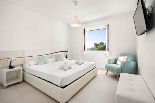 a white bedroom with a bed and a blue chair at Villa Alba by Menorca Vacations in Son Bou